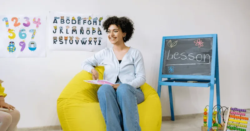 A woman sitting in a nursery room with an alphabet chart and a chalkboard behind her.