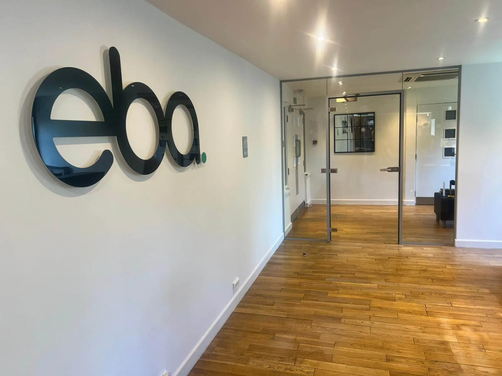 The eba logo mounted on the wall of the refreshed office hallway in Knutsford, with new flooring and glazed doors.