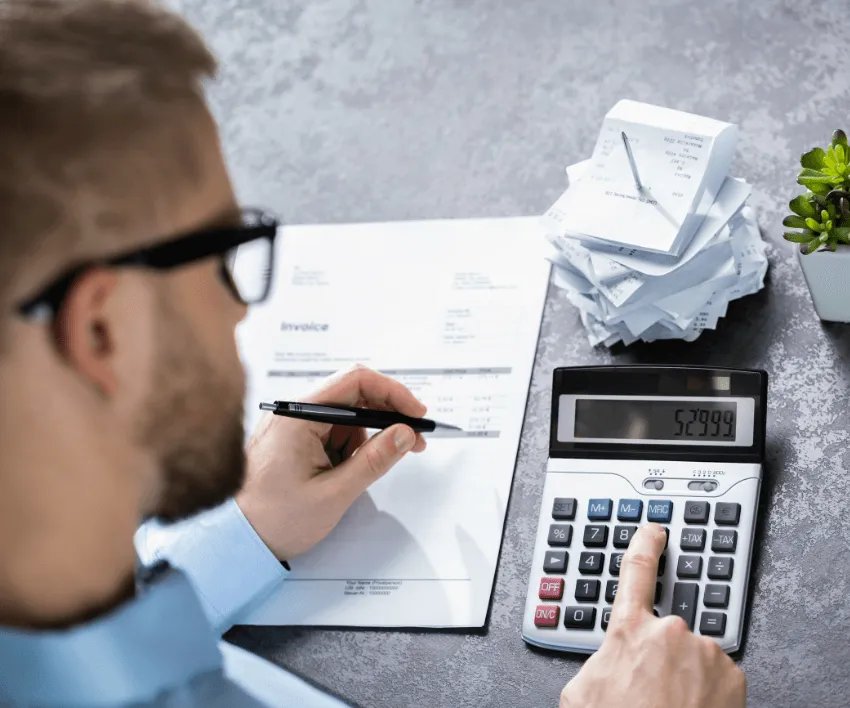A man using a calculator to add up a pile of crumpled receipts on a desk.