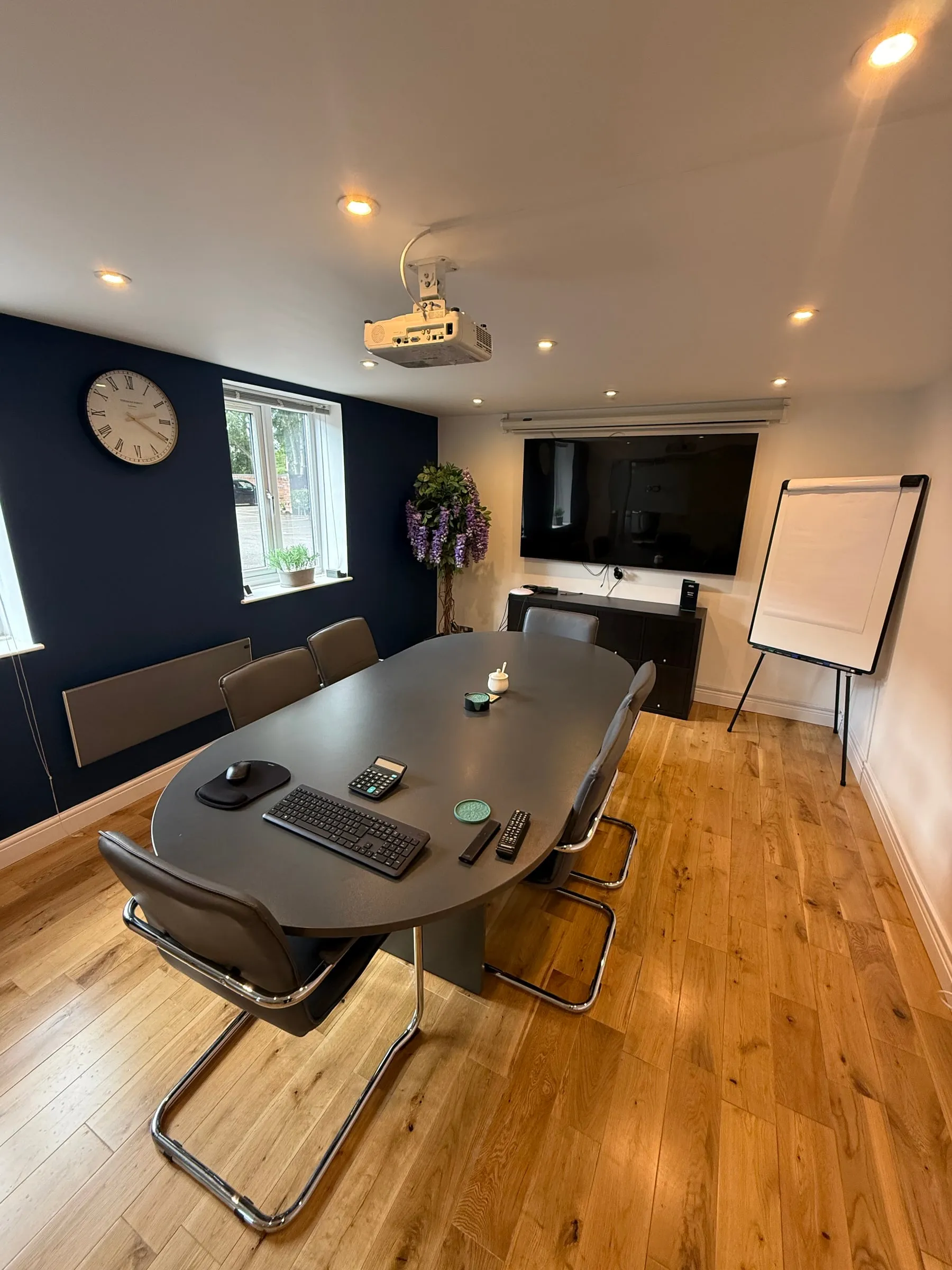 A meeting room at eba with an oval table, a wall mounted screen and a flip chart