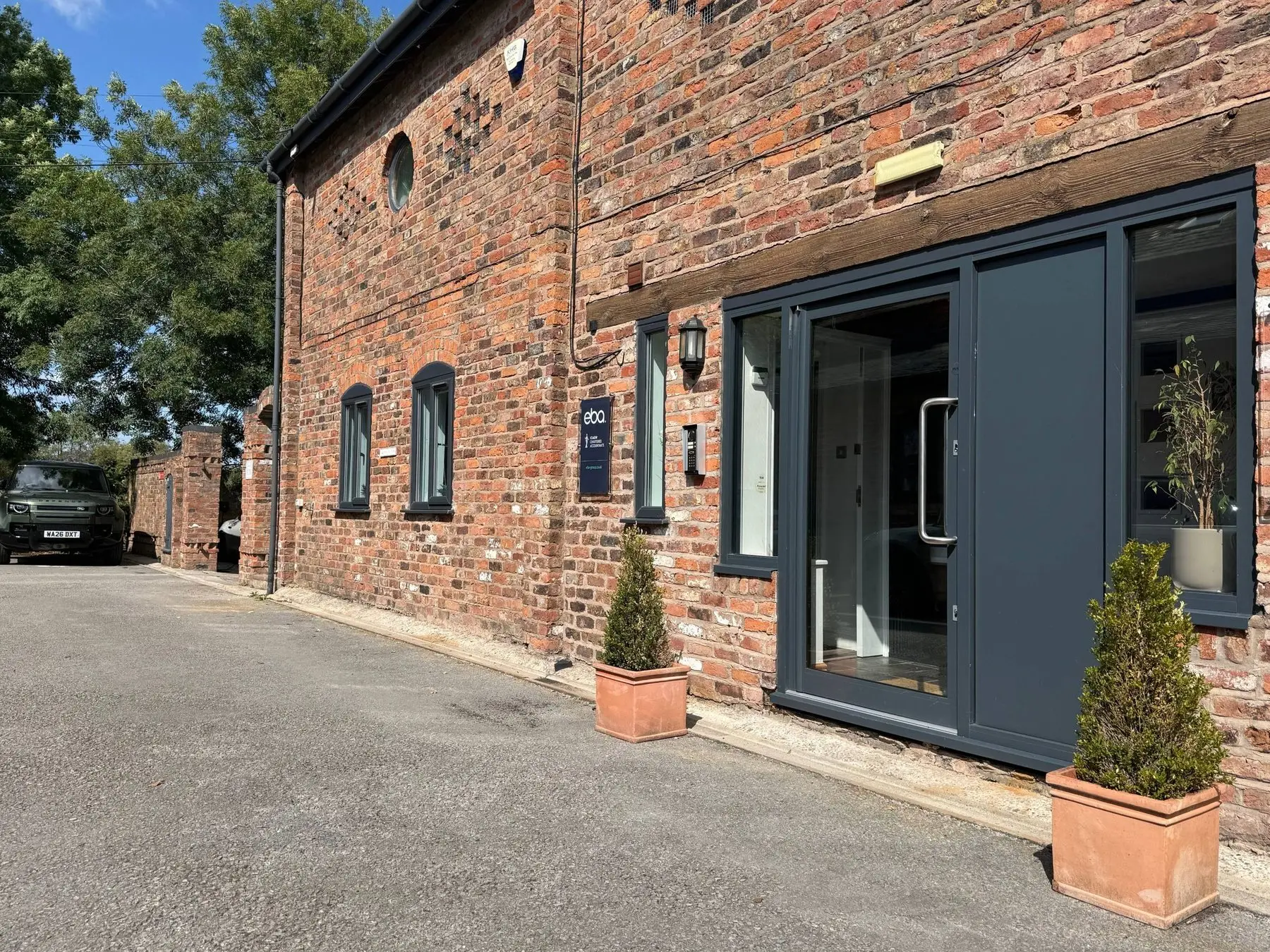 The eba office in Knutsford, Cheshire: a converted red brick barn with the navy eba sign beside the entrance, under a clear blue sky