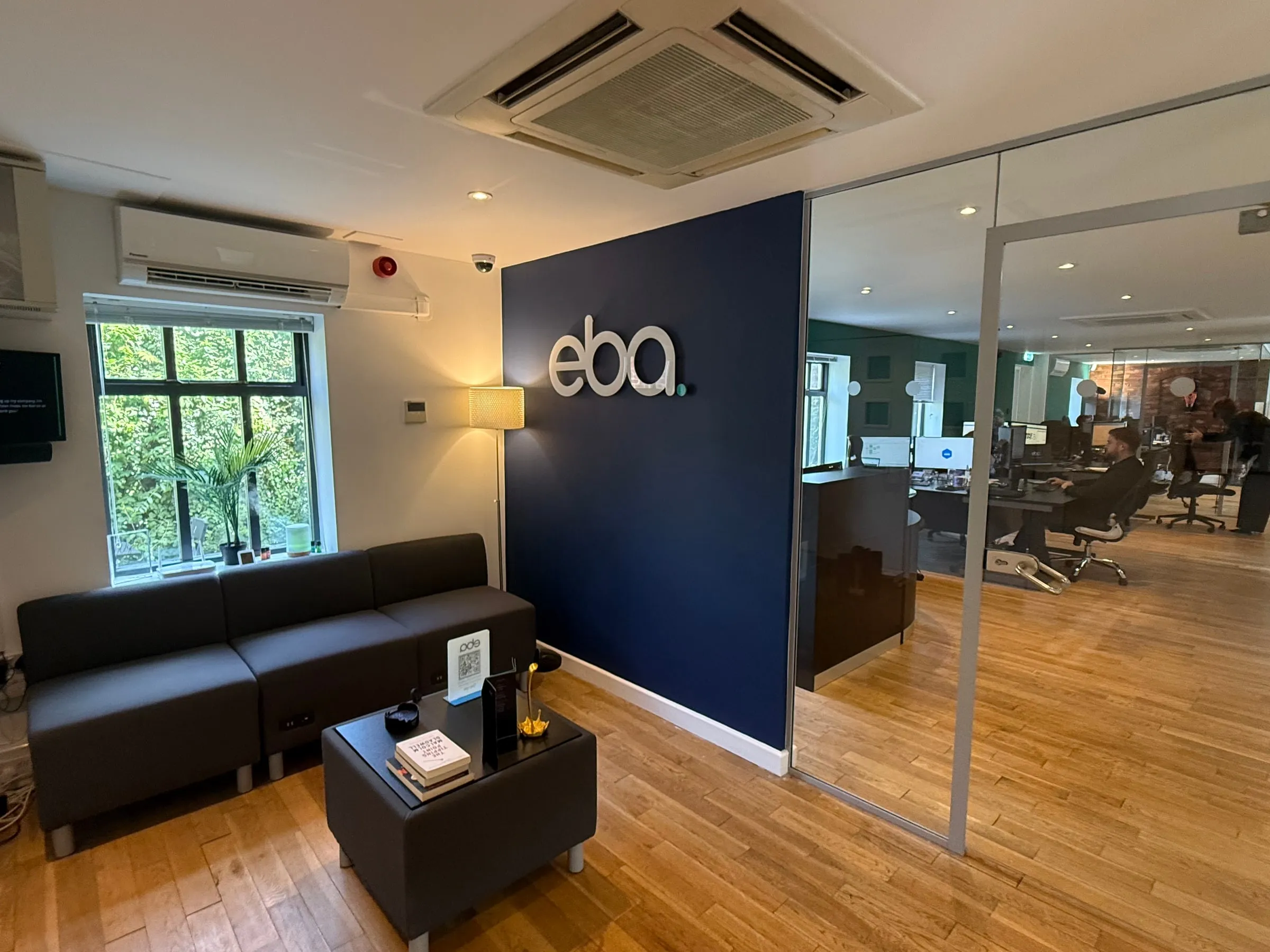 The eba reception: a navy wall carrying the eba wordmark, seating to one side and the open plan office visible through a glazed partition