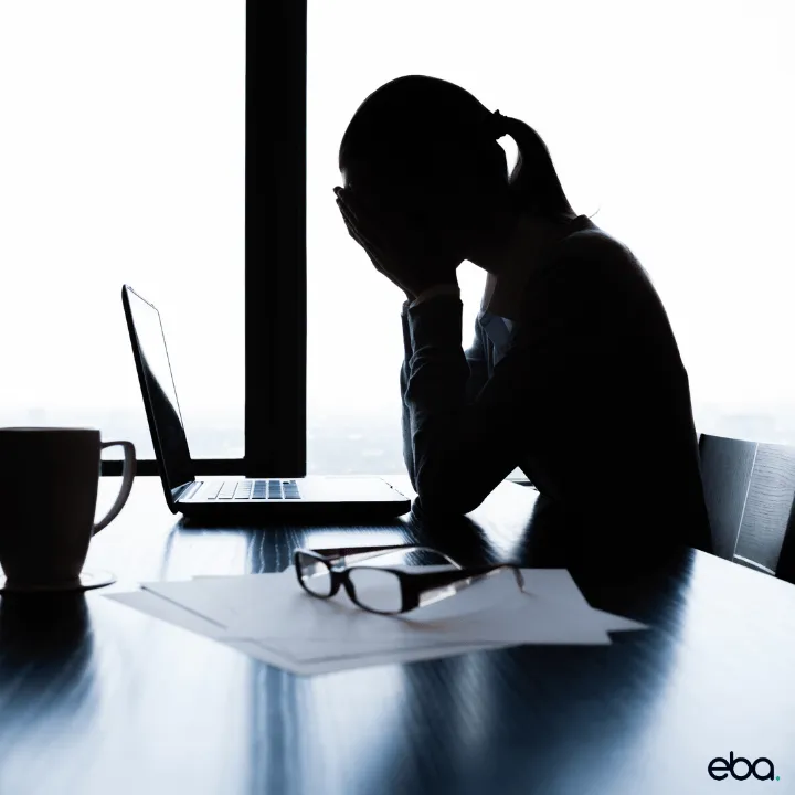 The silhouette of a person sitting at a computer desk with their head in their hands.